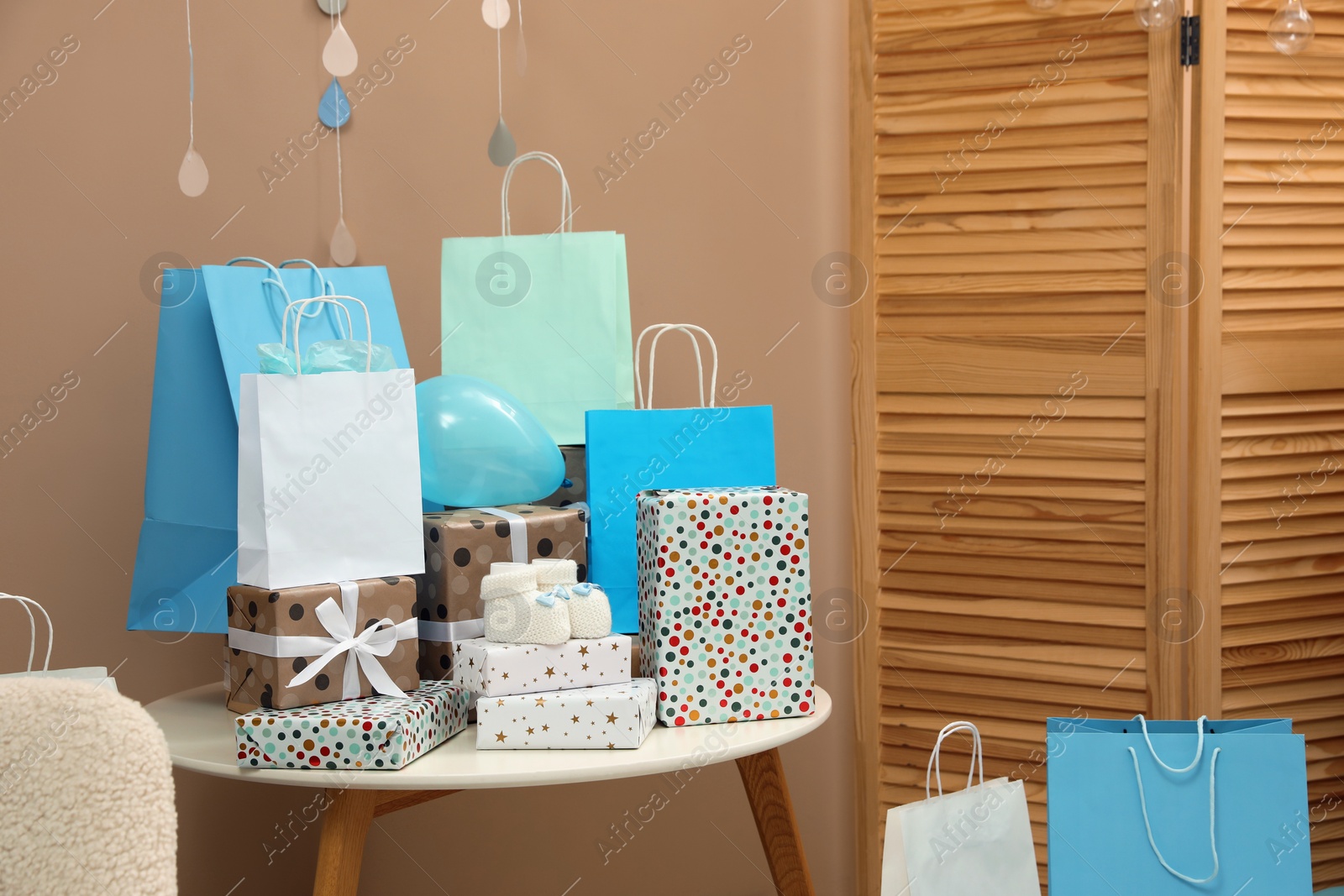 Photo of Baby shower party. Booties, many gift boxes and bags on table in decorated room