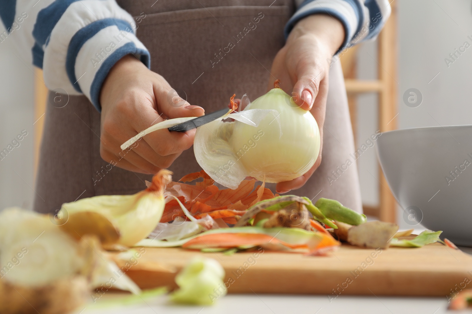 Photo of Woman peeling fresh onion with knife at white table indoors, closeup