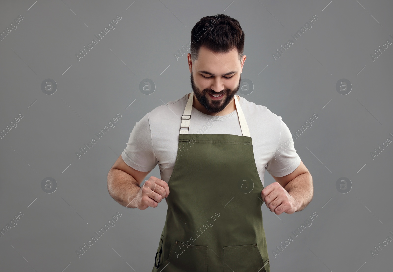 Photo of Smiling man in kitchen apron on grey background. Mockup for design