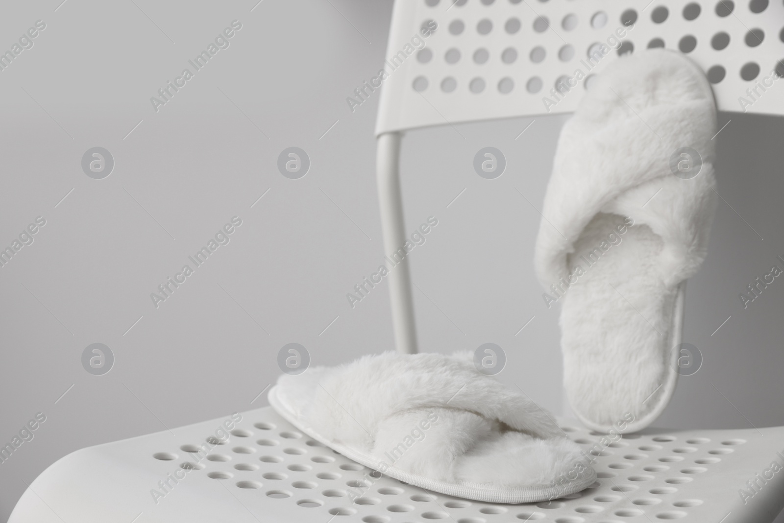 Photo of Soft white slippers on chair, space for text