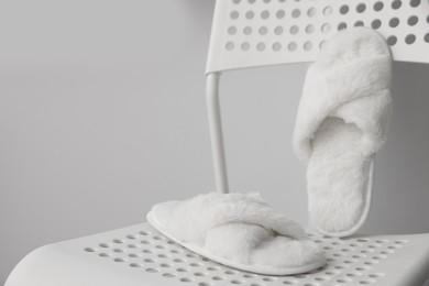 Photo of Soft white slippers on chair, space for text