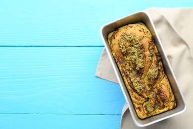 Photo of Freshly baked pesto bread in loaf pan on light blue wooden table, top view. Space for text