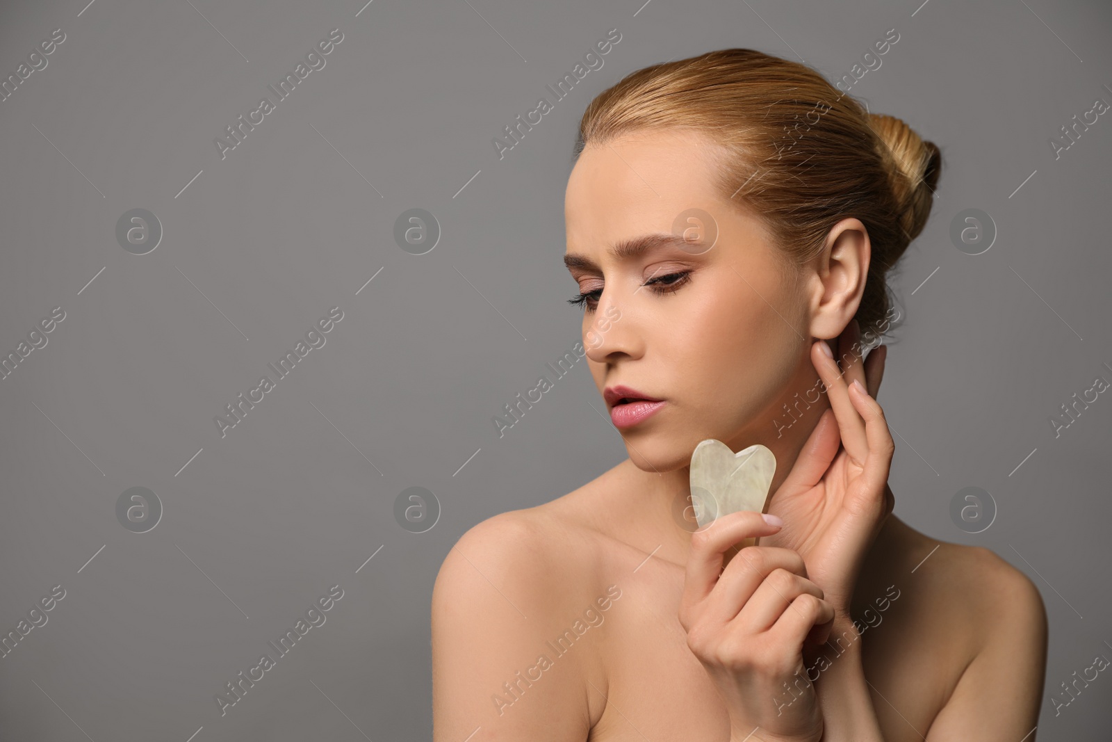 Photo of Beautiful young woman doing facial massage with gua sha tool on grey background. Space for text