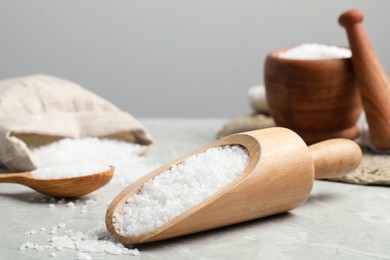 Photo of Natural sea salt in wooden scoop on light grey marble table, closeup