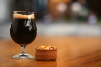 Glass of cold tasty dark beer served with peanuts on wooden table