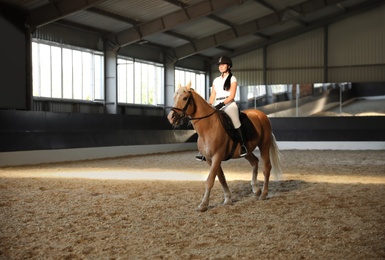 Young woman in equestrian suit riding horse indoors. Beautiful pet