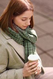 Photo of Beautiful woman in warm scarf with paper cup of coffee outdoors