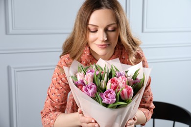 Photo of Happy young woman with bouquet of beautiful tulips indoors