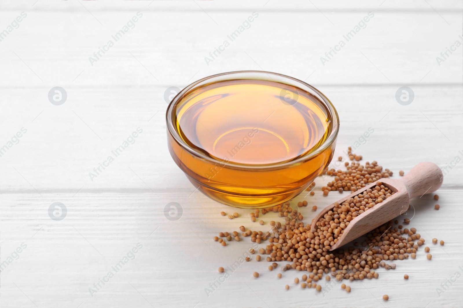 Bowl of natural oil and scoop with mustard seeds on white wooden table Photo of Bowl of natural oil and scoop with mustard seeds on white wooden table