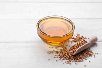 Photo of Bowl of natural oil and scoop with mustard seeds on white wooden table