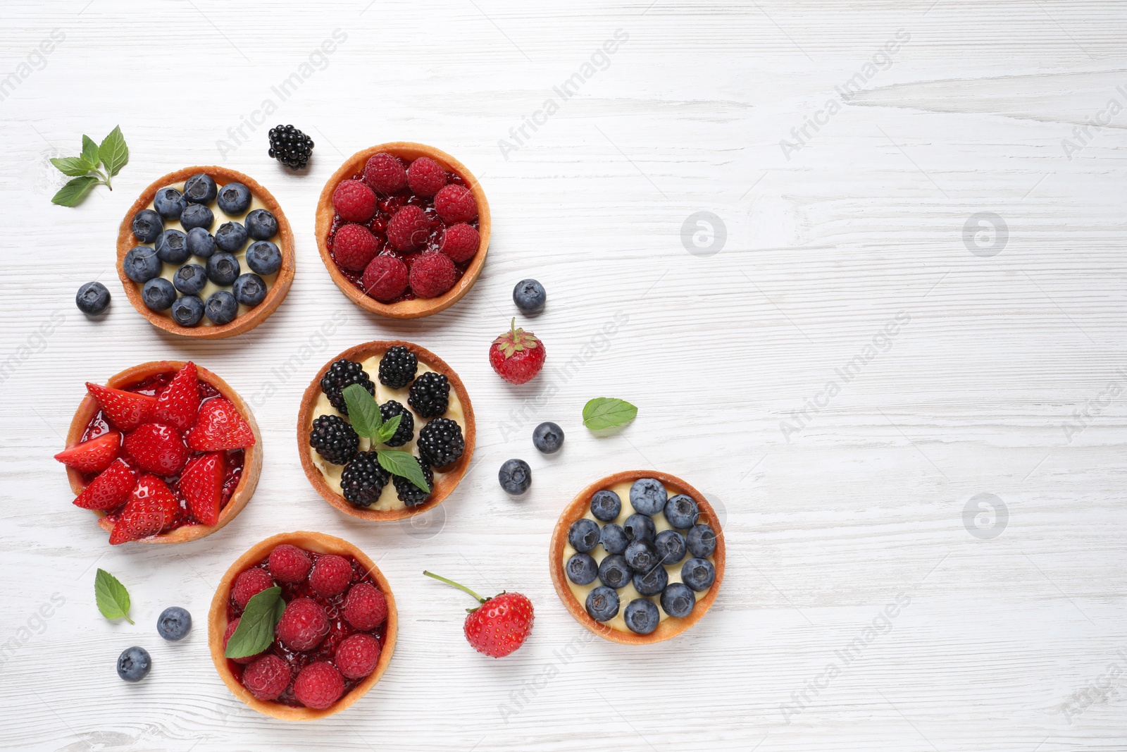 Photo of Tartlets with different fresh berries on white wooden table, flat lay and space for text. Delicious dessert