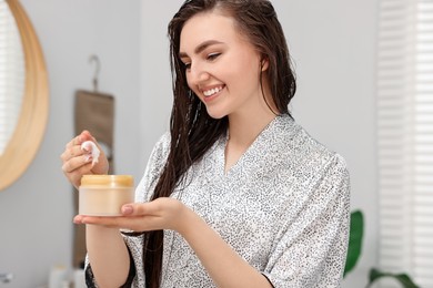 Photo of Young woman with jar of hair mask in bathroom