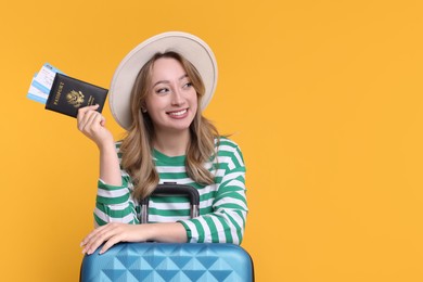 Happy young woman with passport, ticket and suitcase on yellow background, space for text