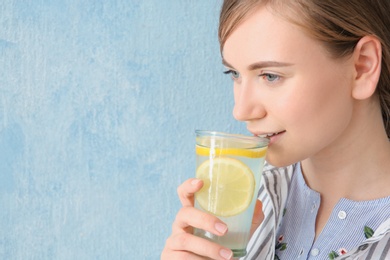 Young woman drinking water with lemon against color background
