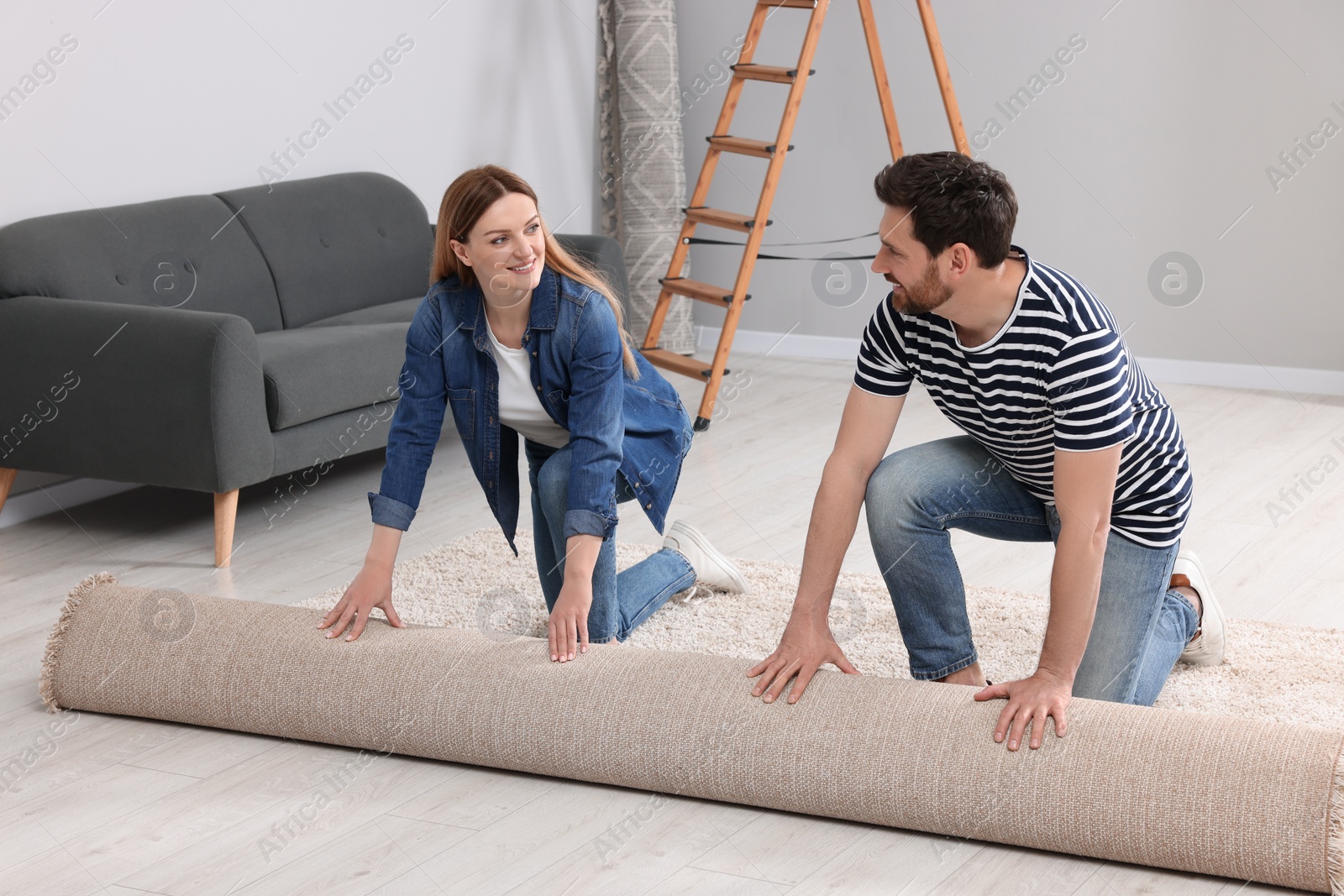 Photo of Smiling couple unrolling new carpet in room