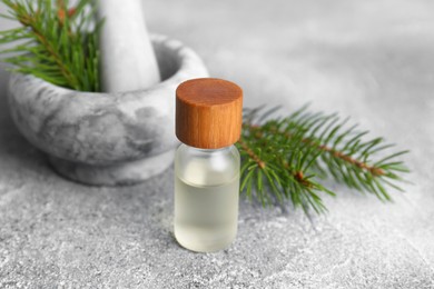 Photo of Bottle of aromatic essential oil and mortar with pine branch on light grey table, closeup