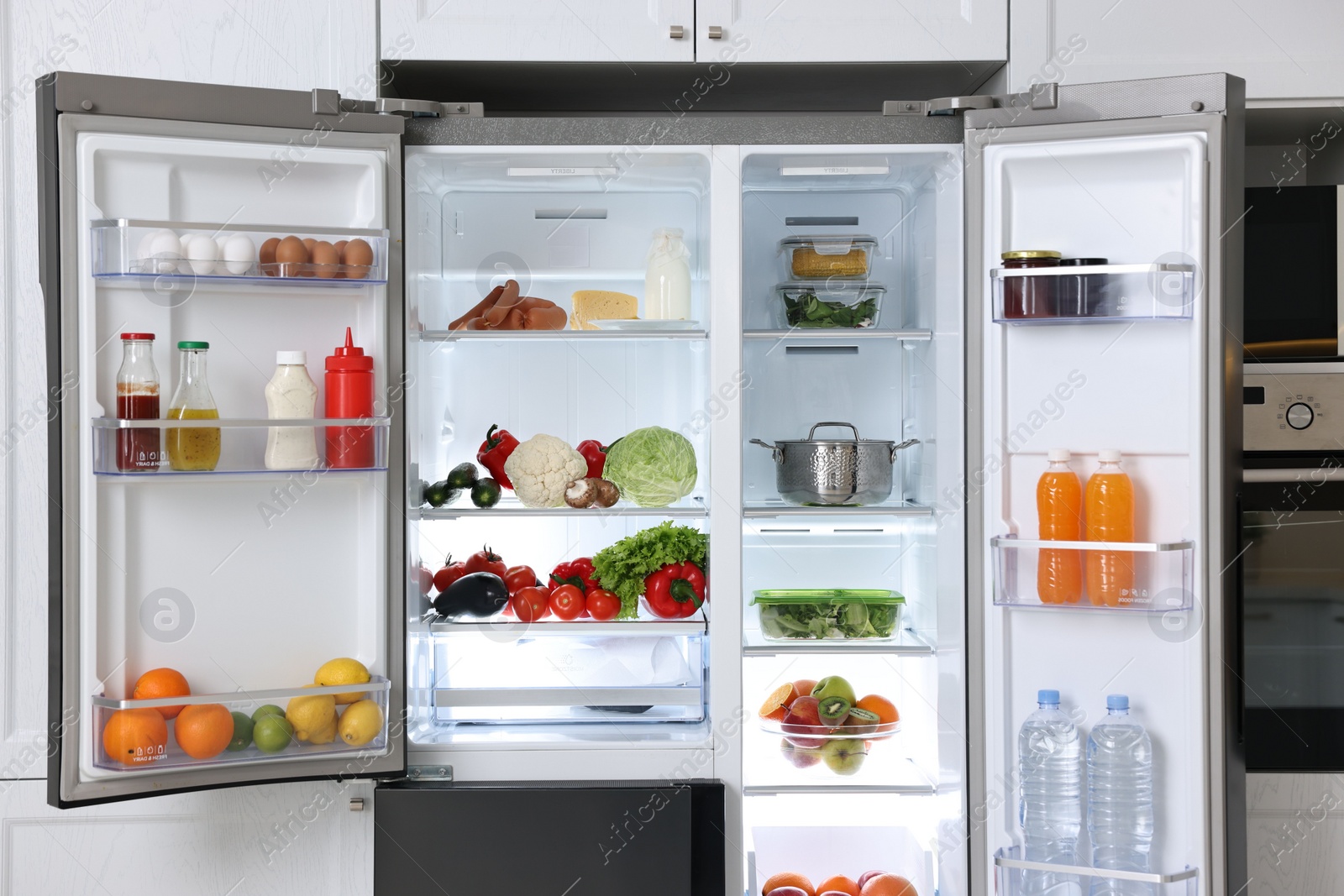 Photo of Open refrigerator full of different products in kitchen