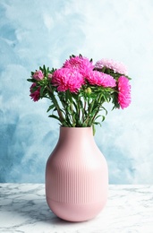 Vase with beautiful aster flower bouquet on marble table against color background