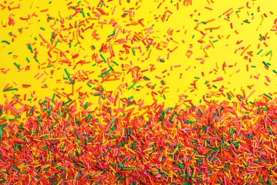 Photo of Bright colorful sprinkles on yellow background, flat lay. Confectionery decor