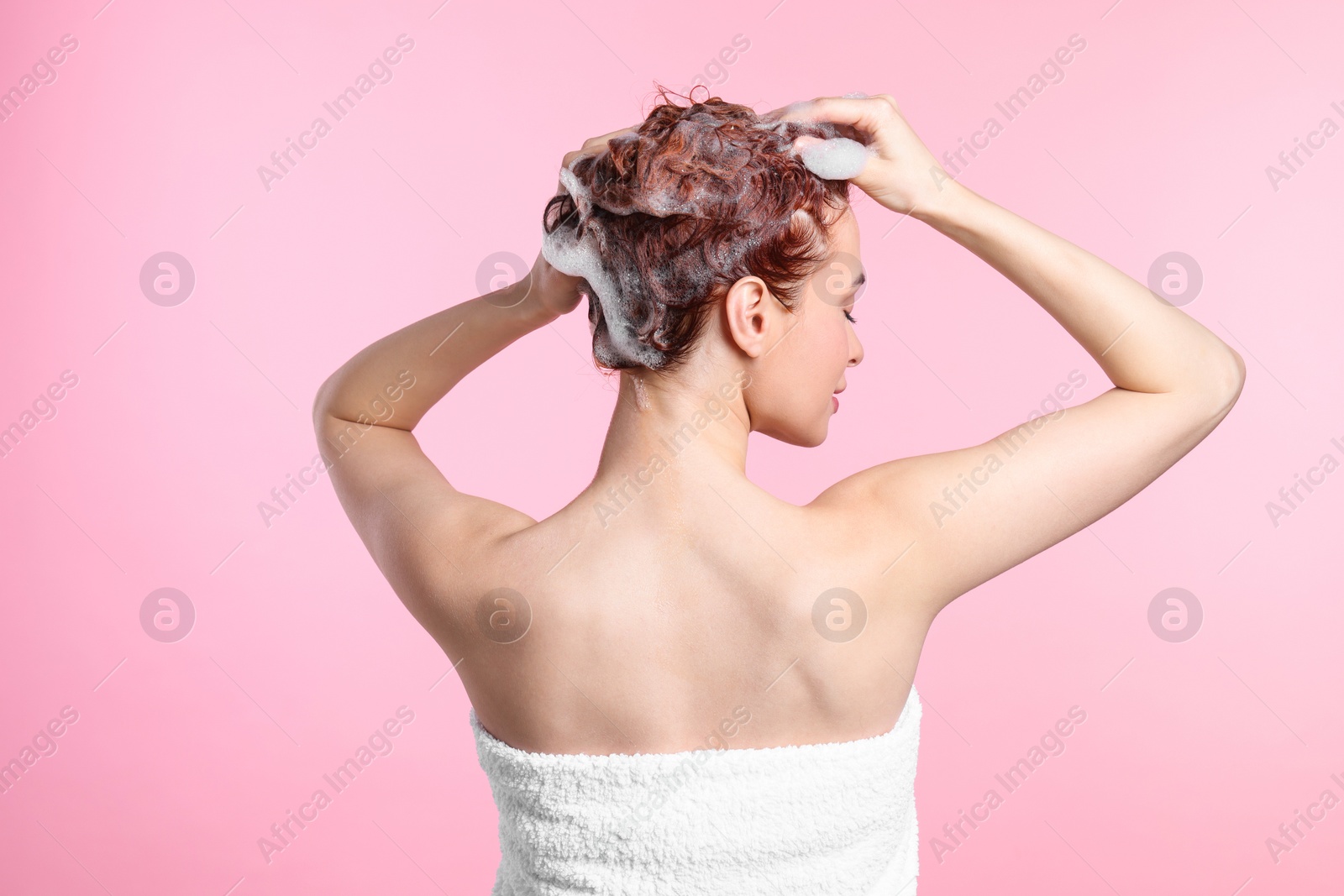 Photo of Young woman washing her hair with shampoo on pink background, back view