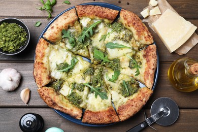 Photo of Delicious pizza with pesto, cheese and arugula served on wooden table, flat lay
