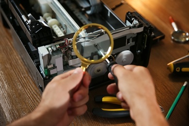 Photo of Repairman with magnifying glass and screwdriver fixing modern printer, closeup