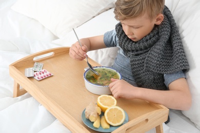 Photo of Sick little boy eating broth to cure cold in bed at home