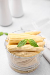 Photo of Canned baby corns with basil on light grey table, closeup