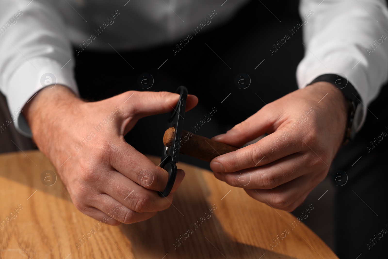 Photo of Man cutting tip of cigar at wooden table, closeup