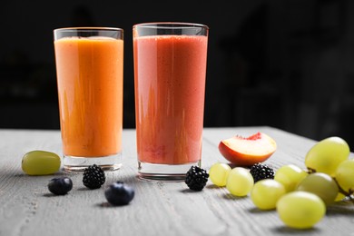 Photo of Different delicious smoothies and ingredients on grey wooden table against dark background