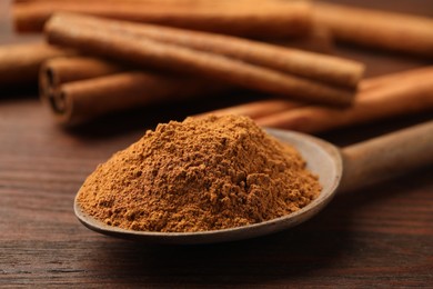 Photo of Spoon with cinnamon powder and sticks on wooden table, closeup