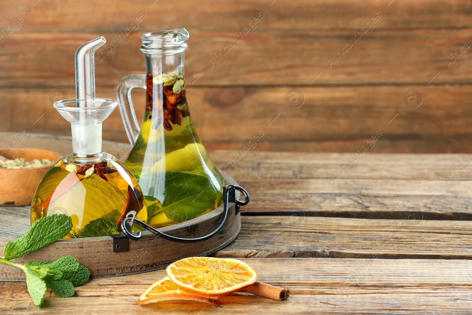 Photo of Cooking oil with different spices and herbs in jugs on wooden table. Space for text