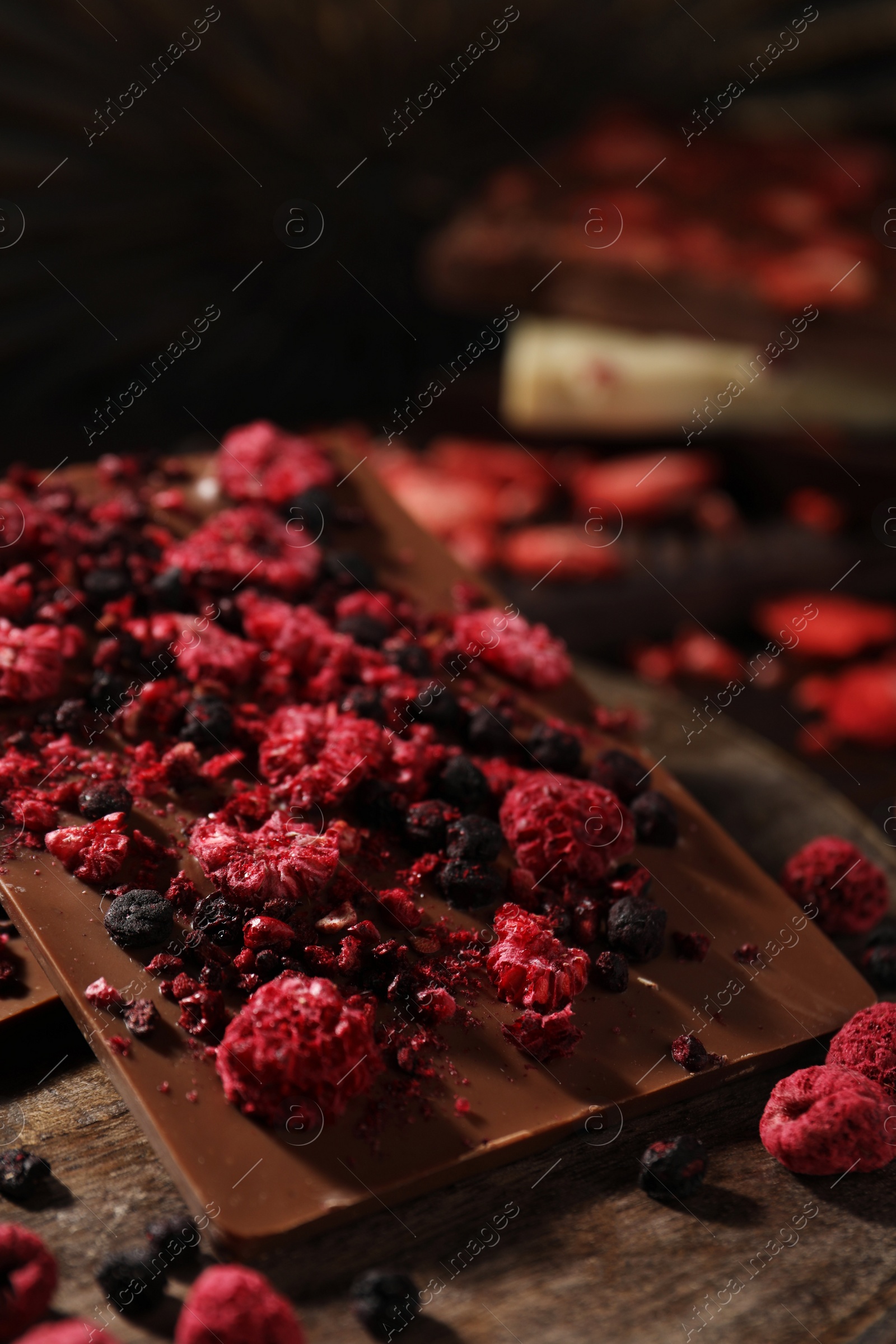 Photo of Chocolate bars with different freeze dried fruits on wooden board, closeup