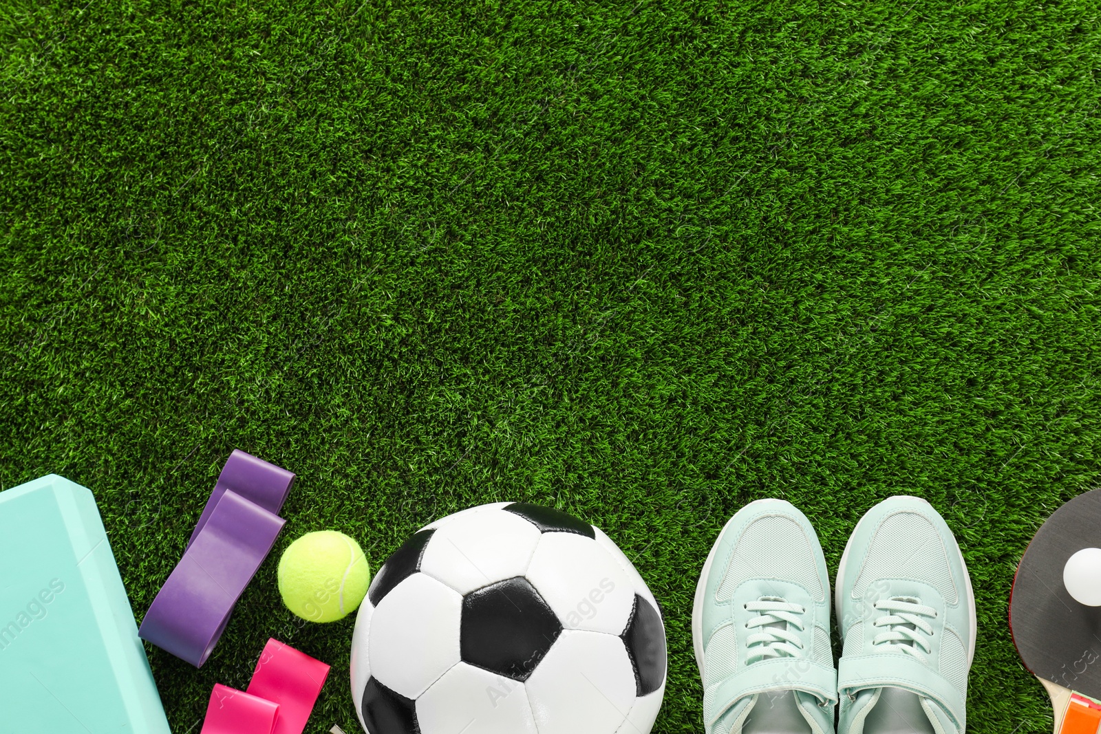 Photo of Different sport equipment and sneakers on green grass, flat lay. Space for text