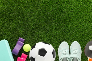 Photo of Different sport equipment and sneakers on green grass, flat lay. Space for text