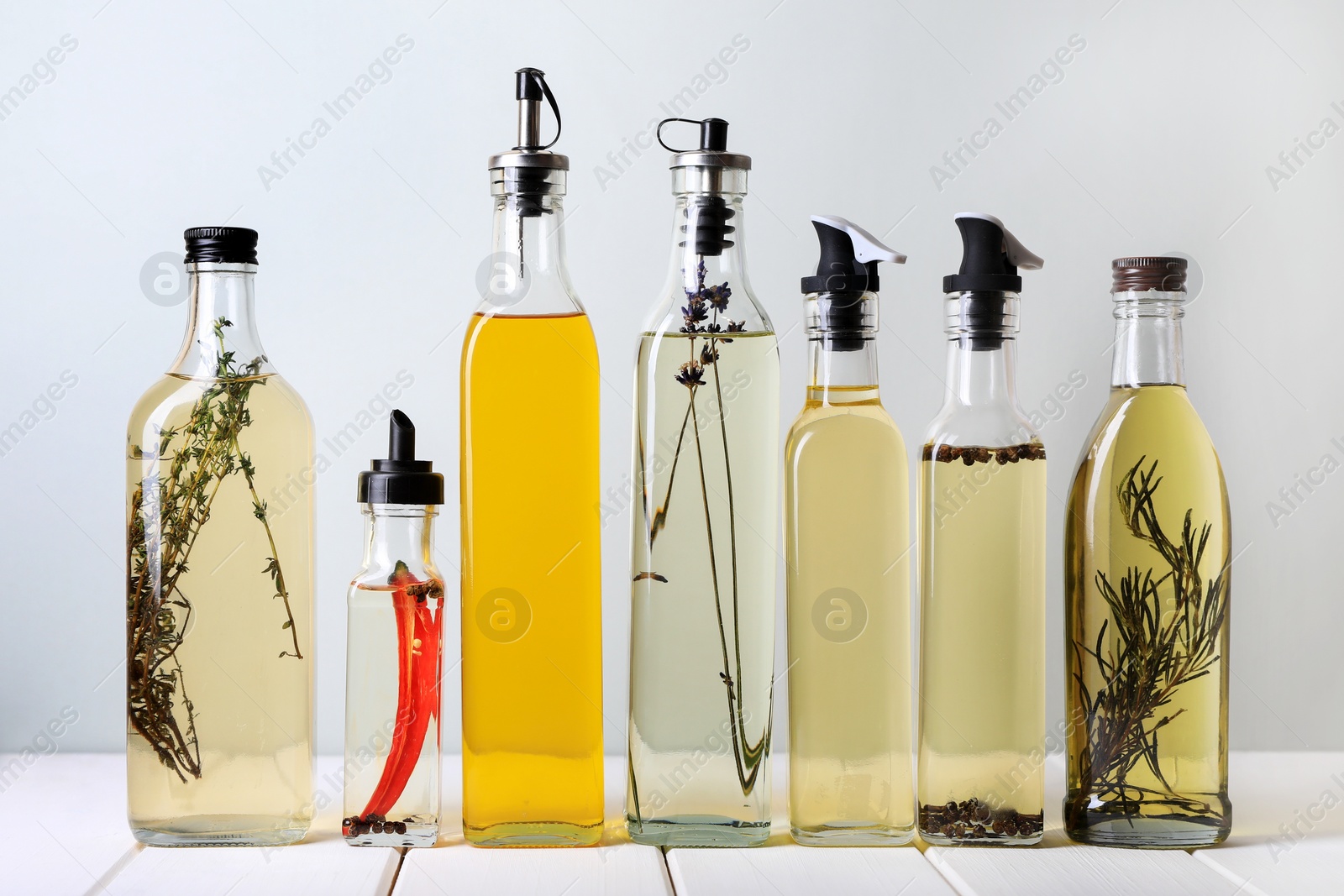 Photo of Bottles of different cooking oils on white wooden table against light background