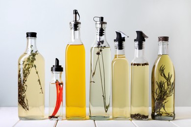 Bottles of different cooking oils on white wooden table against light background