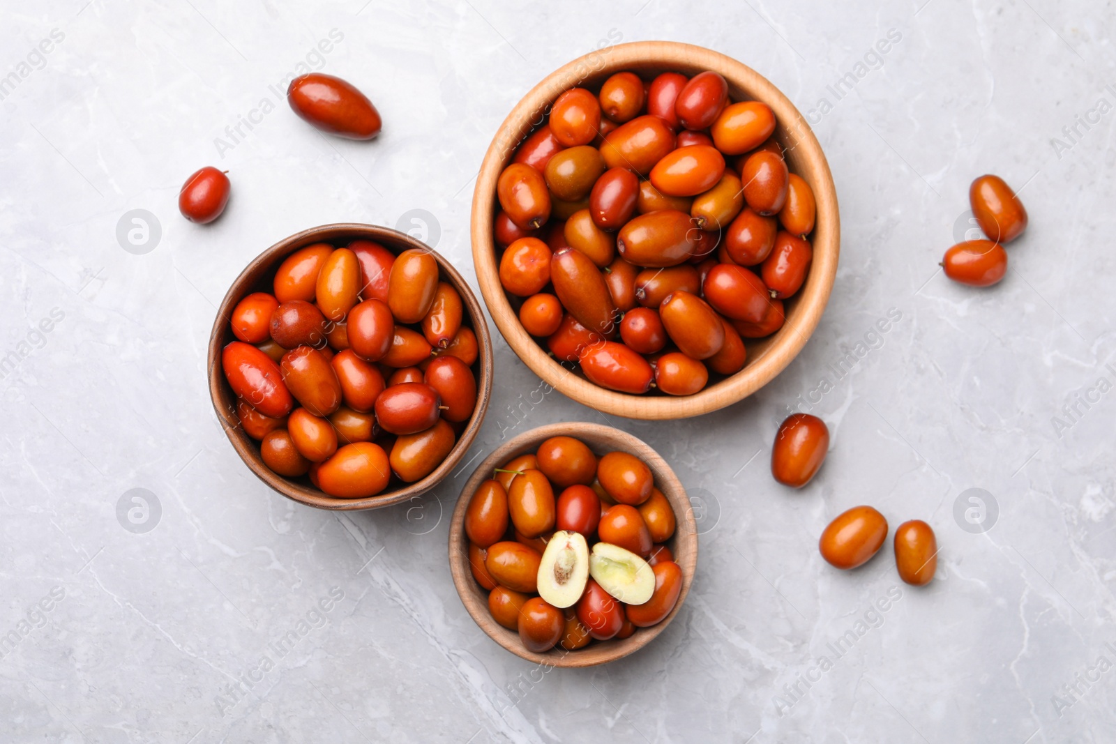 Photo of Fresh Ziziphus jujuba fruits with wooden bowls on light table, flat lay