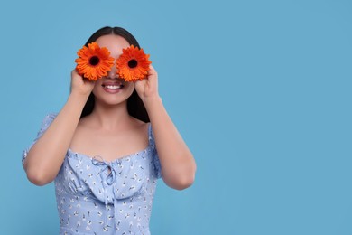 Woman covering her eyes with spring flowers on light blue background, space for text