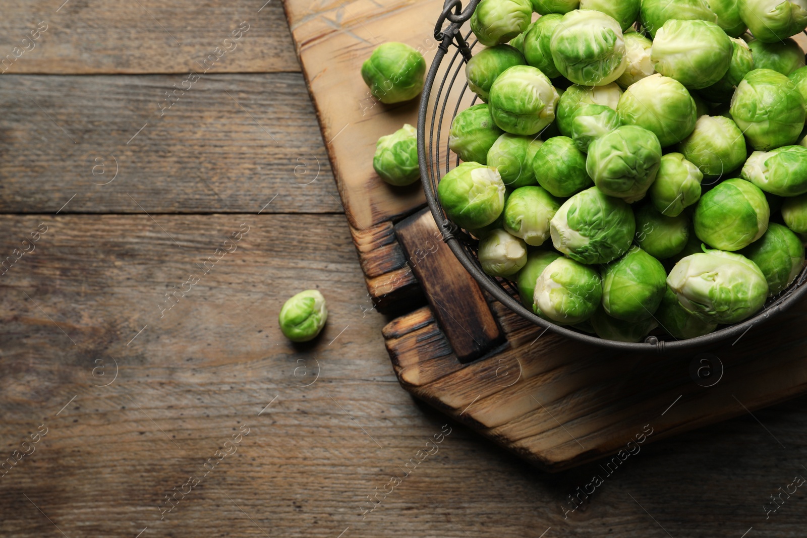 Photo of Metal basket with fresh Brussels sprouts on wooden background, top view. Space for text