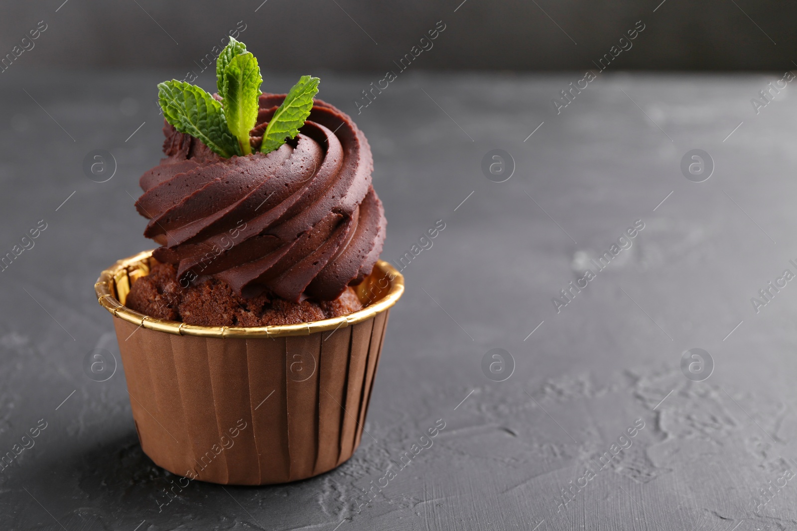 Photo of Delicious chocolate cupcake with mint on black textured table, closeup. Space for text