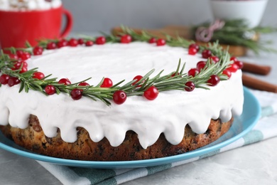 Photo of Traditional Christmas cake decorated with rosemary and cranberries on light grey marble table, closeup