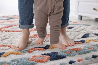 Mother supporting her baby son while he learning to walk on carpet indoors, closeup