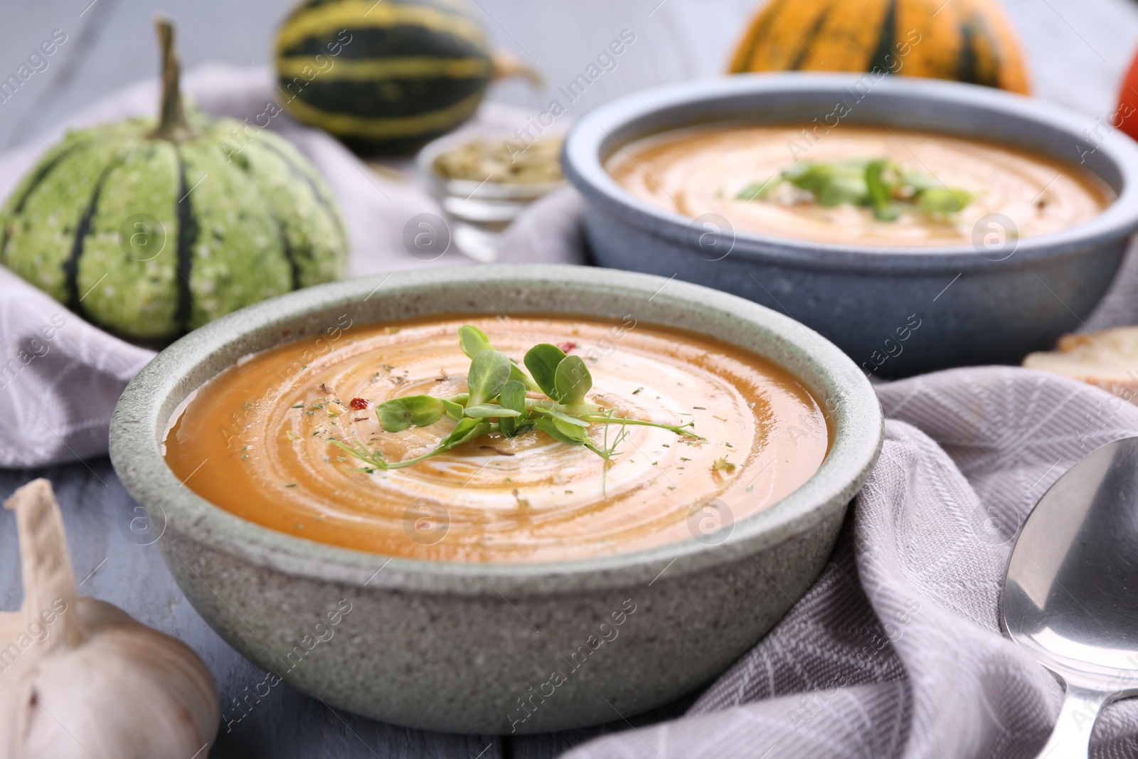 Photo of Delicious pumpkin soup with microgreens in bowls on table, closeup