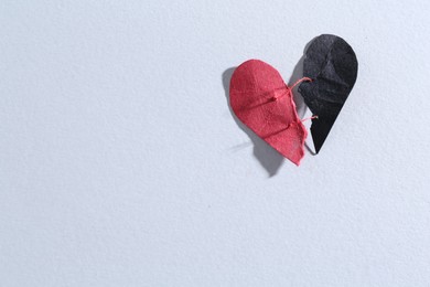 Halves of torn paper heart connected by thread on gray background, top view and space for text. Relationship problem concept