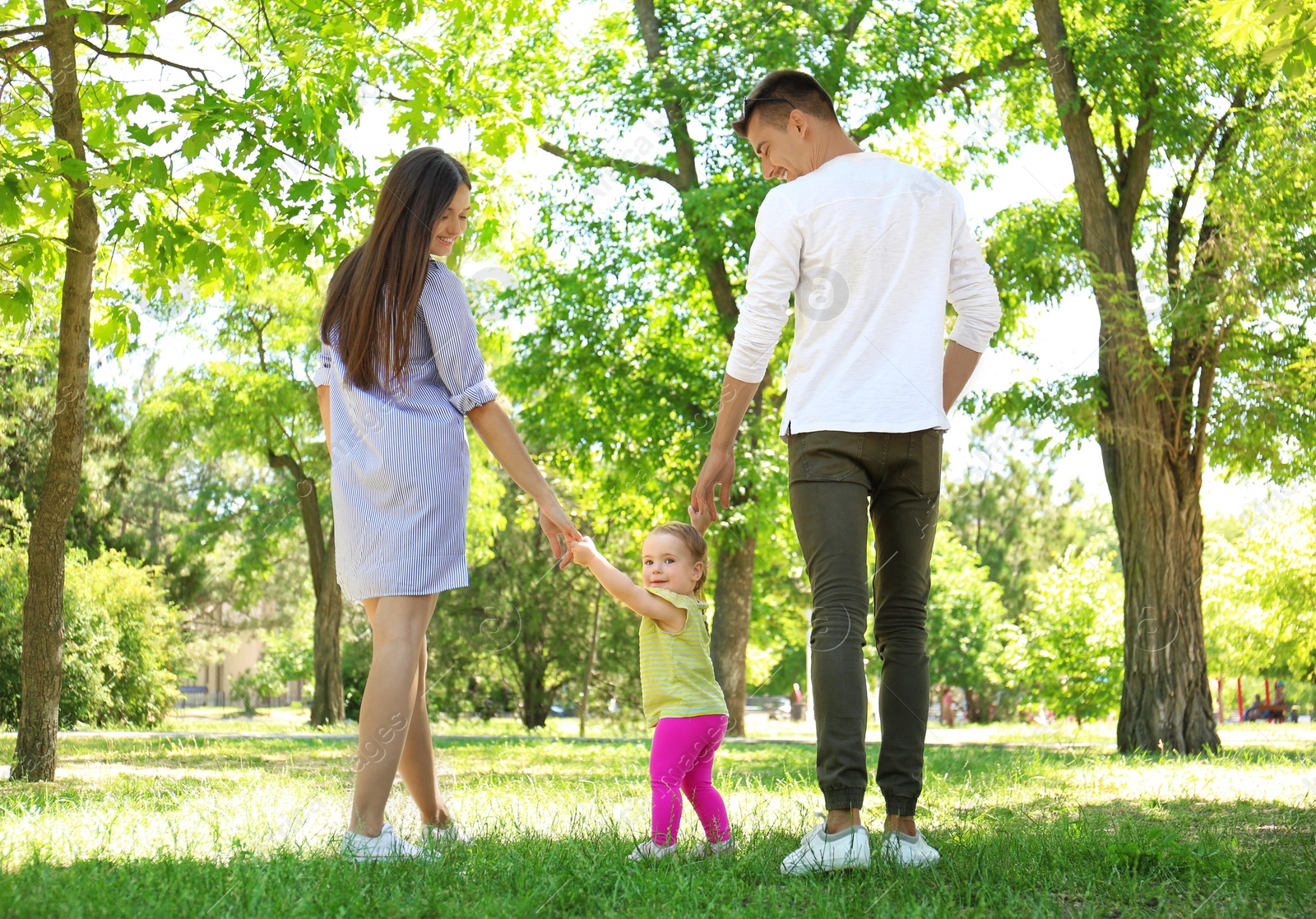 Photo of Parents supporting their baby daughter while she learning to walk outdoors