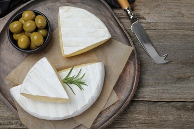 Photo of Tasty cut brie cheese with rosemary and olives on wooden table, flat lay