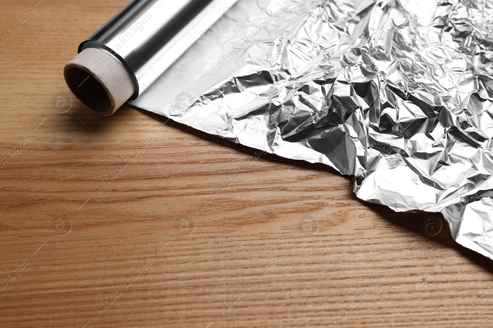 Photo of Roll of aluminum foil on wooden table, closeup. Space for text