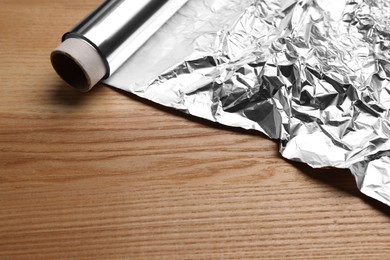 Photo of Roll of aluminum foil on wooden table, closeup. Space for text