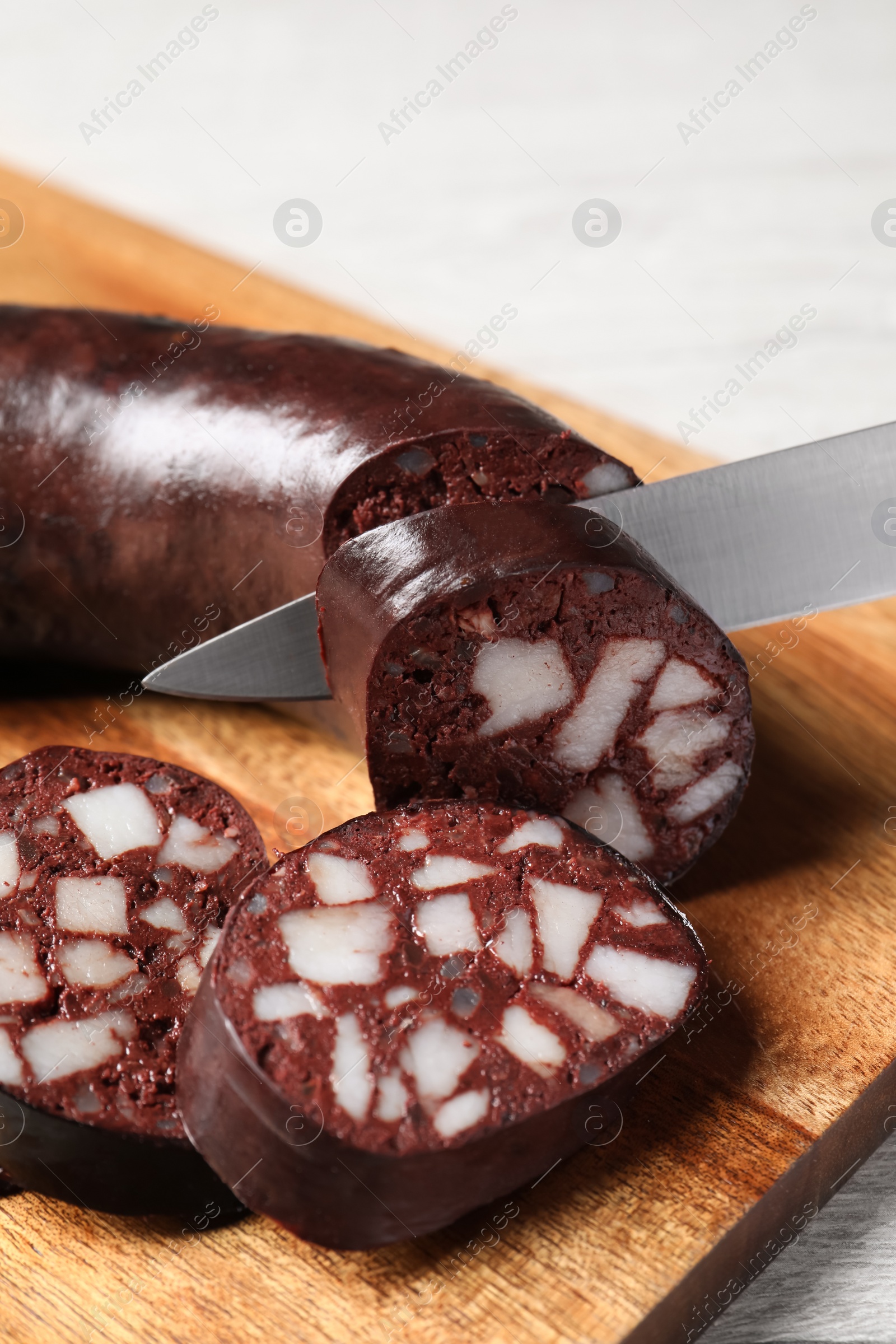 Photo of Cutting tasty blood sausage on wooden board, closeup